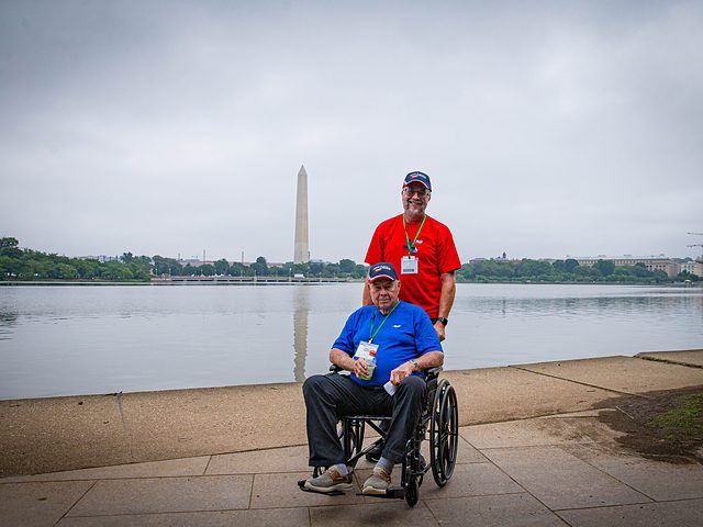 Guardian standing with a veteran in a wheelchair across from the Washington Monument